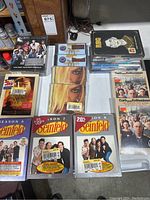 Photo showing multiple sealed DVDs including Seinfeld Seasons 5, 6, 7, boxed sets, and CDs, arranged on a table.