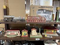 Shelf showing Lionel silver tank train car, red metal bridge, and multiple metal buildings including diner car and other painted structures