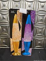 Two lava lamps in original boxes showing front images of a yellow and a blue glitter lamp.