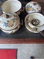 Photo showing the entire enamelware lot including three pots with floral designs, two lids with brass knobs, and the fondue warmer with burner.