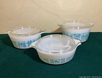 Three Pyrex Amish Butterprint dishes with lids shown side by side, displaying size variation and blue pattern on white glass.