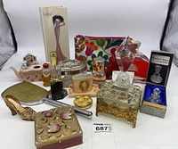 Full view of assorted vintage woman’s vanity items including perfume bottles, trinket dishes, compact mirror, and decorative containers arranged together.