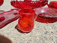 Close-up of the small amber glass pitcher with controlled air bubbles and several red glass bowls and trays around it