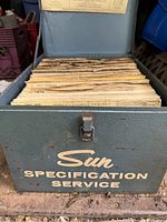 Metal box with Sun Specification Service on front, filled with stacked aged specification sheets.