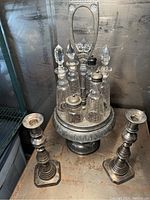 Angle showing full cruet set on ornate metal stand with glass bottles and push-up candlesticks on either side