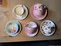 Five fine bone china cups and saucers displayed on wooden table showing variety of patterns and colors