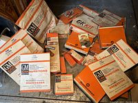 Multiple original packaging boxes, kits, and manuals for Delco GM Rochester carburetor parts from 1957, displayed on wooden surface.