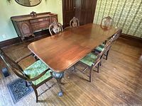 Wide-angle showing entire dining set with six chairs and table with two leaves extended in formal room with sideboard in background.