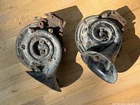 Pair of snail-style spiral early car horns with metal mounting brackets and surface rust.