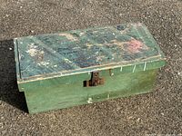 Front angled shot of the wooden tool box showing worn green paint and metal latch in closed position.