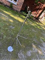 Full view of the metal adjustable linen and towel rack placed outdoors showing circular base, adjustable horizontal towel bars, and upper coat hooks.