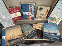 Old brown leather briefcase open showing assorted German ephemera including St. Raphael Kalender from various years, Canadian Scene magazine, and other booklets.