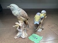 Pair of porcelain bird figurines displayed on floor with green lot number tag
