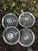 Four Pontiac hubcaps displayed on the ground showing front sides with radial fin design and embossed Pontiac center caps.