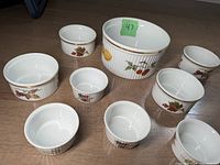 Top-down view of nine Royal Worcester ramekins of three sizes with fruit decoration on a wooden floor