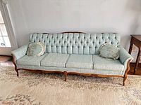 Full-length front view of light blue tufted button back sofa with carved wooden frame and two round accent pillows