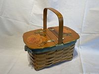 Side angle view of wicker basket showing wooden lid with yellow rose decoupage and central wooden handle.