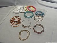 Overview of assorted fashion jewelry bracelets and bangles arranged on white fabric background