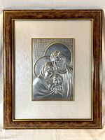Full view of framed religious silver and gold tone relief plaque depicting the Holy Family in wood frame with glass and matting.