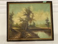 Front view of vintage oil painting landscape in worn wooden frame, showing trees, path, and water under sky.