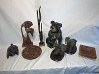 Group of seven wooden decorative items including mask, dial, sculptures, bear figures, elephant bookends, and bowl arranged on white background.