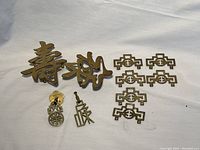 All 7 brass hardware pieces arranged showing two large character plaques, five smaller symmetrical geometric patterned plates, and two small detailed hardware pieces.