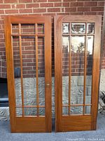 Full view of the two wooden French doors with multiple clear glass panels against a brick wall.