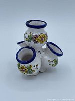 Front angle view of the multi-spout ceramic vase showing yellow floral hand-painted designs and blue rims on white ceramic.