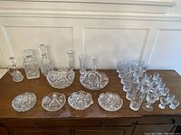 Wide view showing all items in the set arranged on a wooden sideboard: 3 decanters, 3 vases, 6 bowls, and combined glasses.
