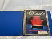 Open blue binder with The New Music magazine visible in protective sleeve, issue cover featuring an empty theater seat.