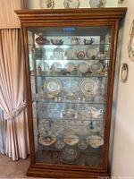 Front view of wood and glass tall display cabinet showing multiple glass shelves and mirrored back filled with decorative items (not included).