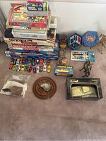 Photo showing a variety of classic board games stacked with Hot Wheels cars and other toys on the floor.