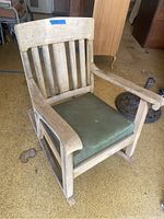 Front view of the vintage wooden rocking chair showing slatted back and green cushioned seat with weathered wood.