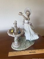 Full view of the Lladro Dancing Birdbath sculpture showing the woman, birdbath with birds, and floral base with a ruler for scale.