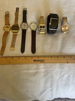 Layout of all 7 men's watches with a ruler for scale, showing variety of styles and bands.