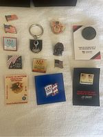 Full view of all 13 Olympic collectible pins arranged on white surface including keychain and pins with various USA Olympic designs.