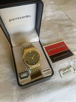 Photo of the watch in original Pierre Cardin box showing watch with black dial, gold tone bracelet, diamond bezel, and included warranty card and tags.