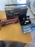 Overview of entire lot showing both boomboxes, CB radio case with cables, and boxed emergency CB pack.