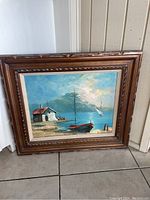 Photo of full framed painting showing coastal scene with boats and a house, wooden carved frame.