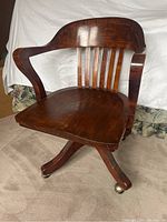 Front angled view of vintage solid wood office chair showing curved backrest, armrests, and four-leg base with casters.