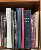 Photo showing 11 books about service and medals lined up vertically on a wooden shelf.