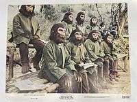 Lobby card showing nine ape characters seated outdoors wearing green tunics