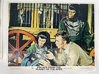 Close-up of lobby card number 3 with ape characters and a man near a wagon wheel