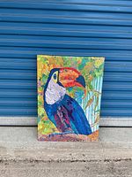 Full view of the colorful toucan bird artwork on stretched canvas against a blue metal background.