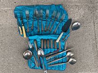 Complete view of Birks stainless steel flatware set laid out on blue fabric roll on pavement.