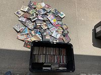 Black plastic tub filled with stacks of CD jewel cases and a pile of loose CDs on concrete