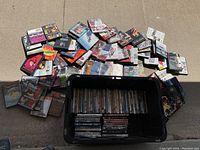 Plastic bin filled with stacked DVDs and approximately 80 DVDs scattered around the bin showing a large variety of titles and cover art.