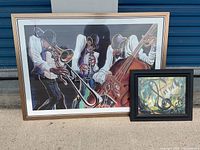 Photo showing both framed artworks side by side outside with storage door background.
