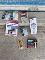 Photo shows 8 miscellaneous household items including three GE timer/outlet products, Vivitar 35mm camera, Kong light bulb adapter, magnifying glass, keychain-like item, and Mastercraft screwdriver set.