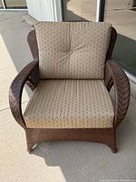 Front view of a brown wicker patio chair with beige striped cushions on seat and backrest.